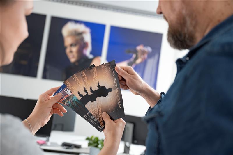 Zwei Männer stehen nebeneinander und halten Konzertkarten in den Händen.